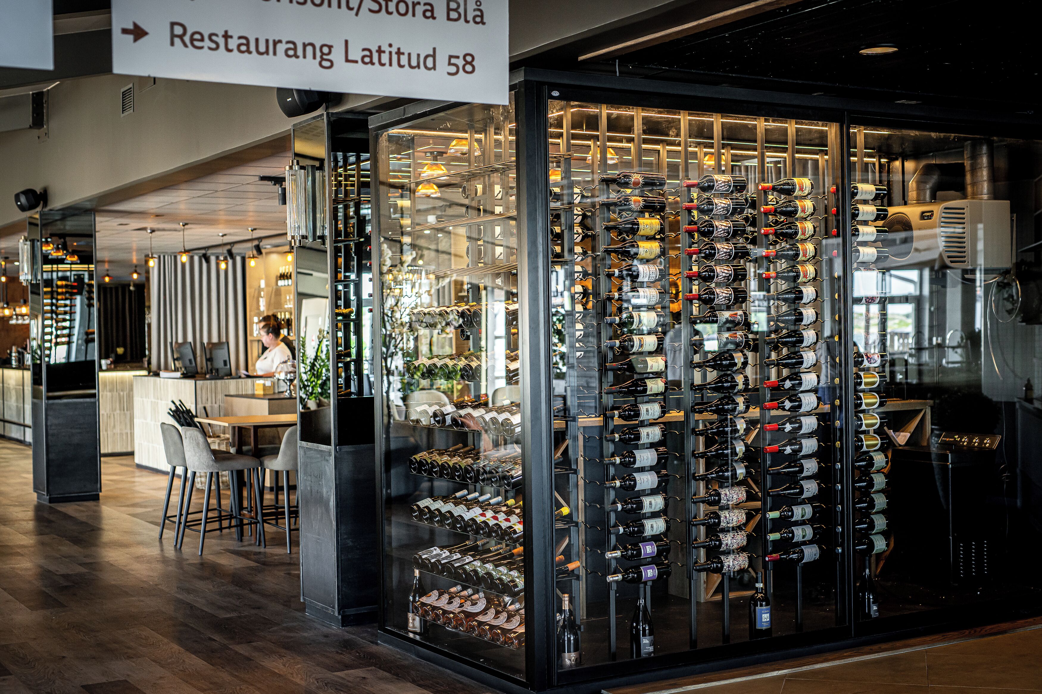 Una tienda de vinos con fachada de vidrio y un letrero que indica la cercanía de un restaurante.
