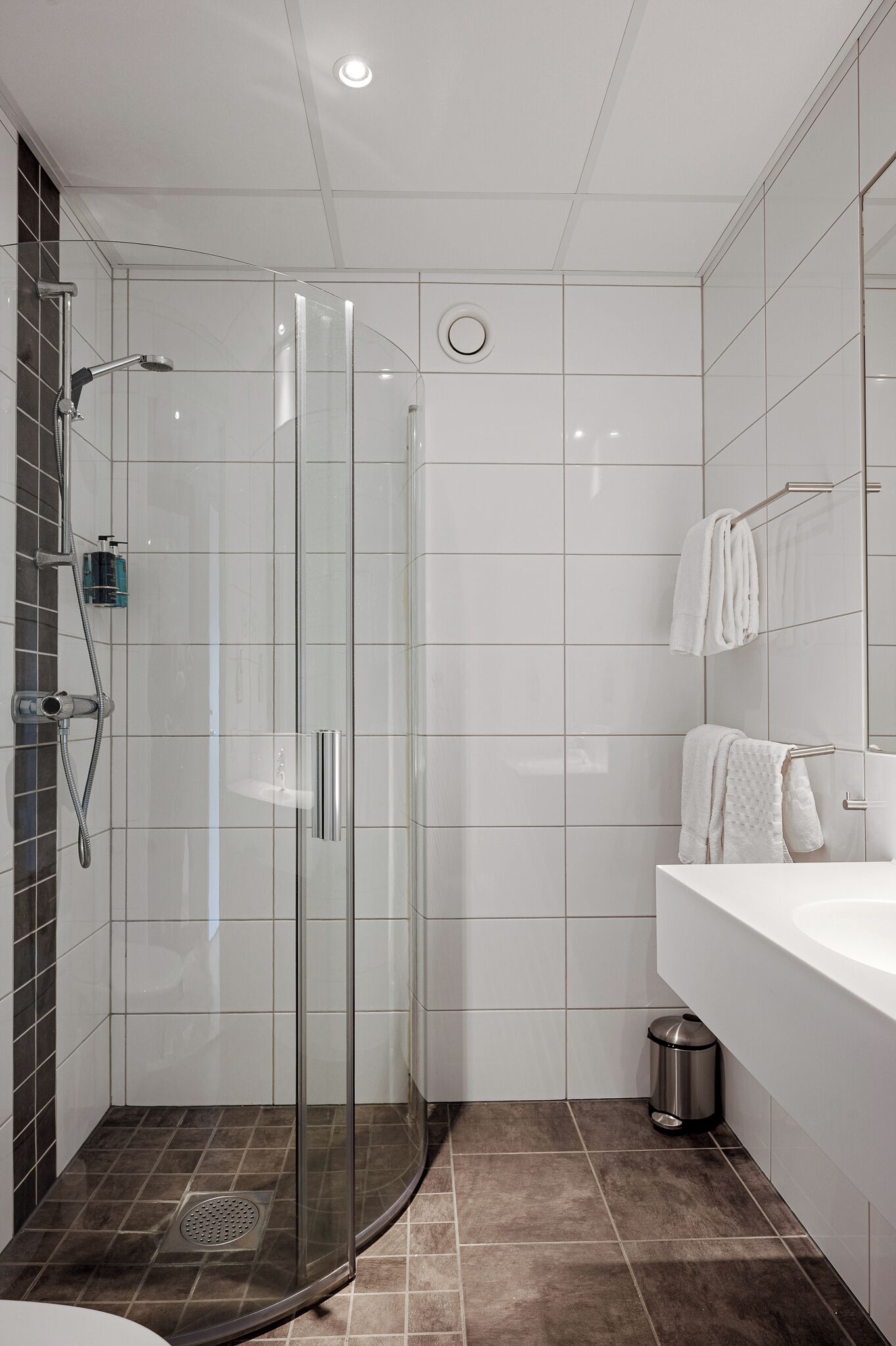 Um banheiro moderno com chuveiro em cabine de vidro, pia branca e piso revestido com azulejos.