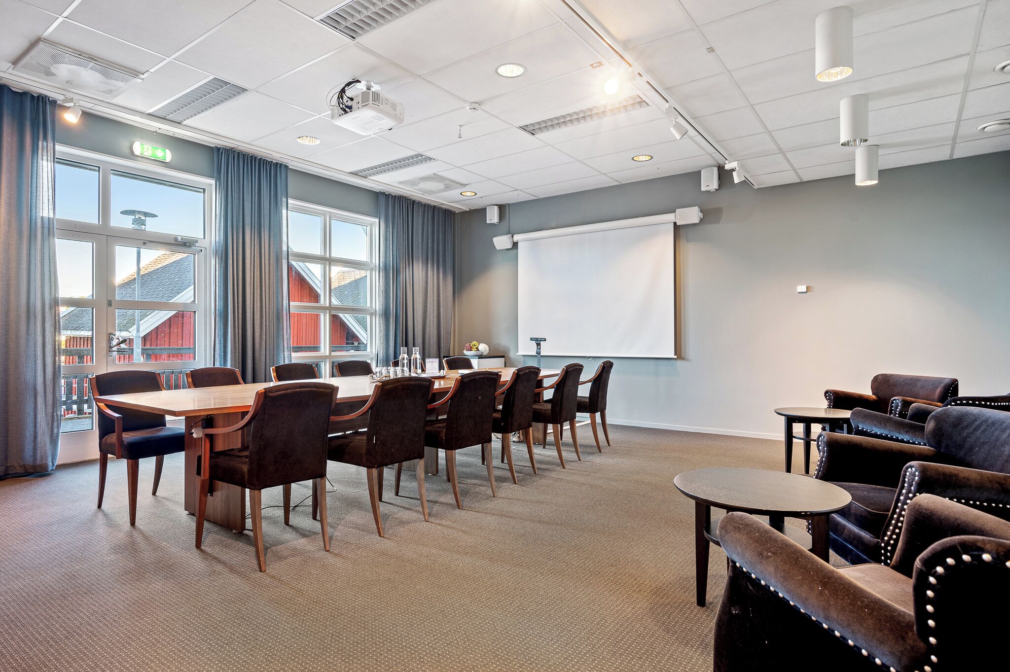 A conference room with a large table, chairs, a projector, and a screen.