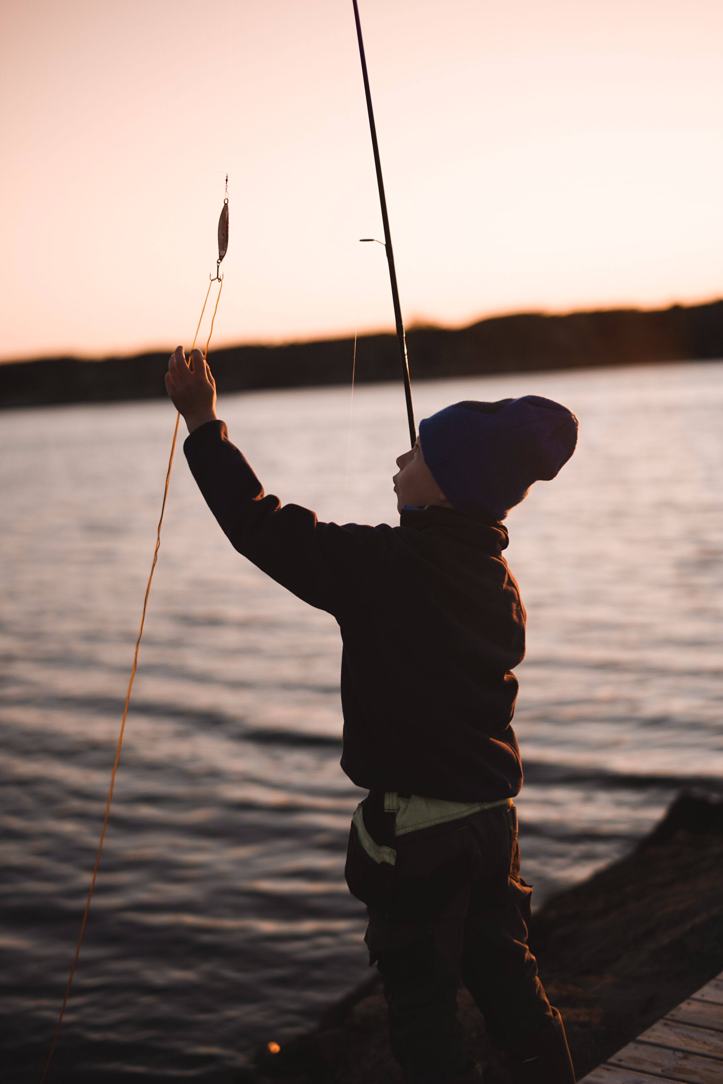 Una persona pescando junto a un cuerpo de agua tranquilo al atardecer.