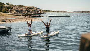 Two people on paddleboards in a calm body of water with a dock and rocky shoreline in the background.