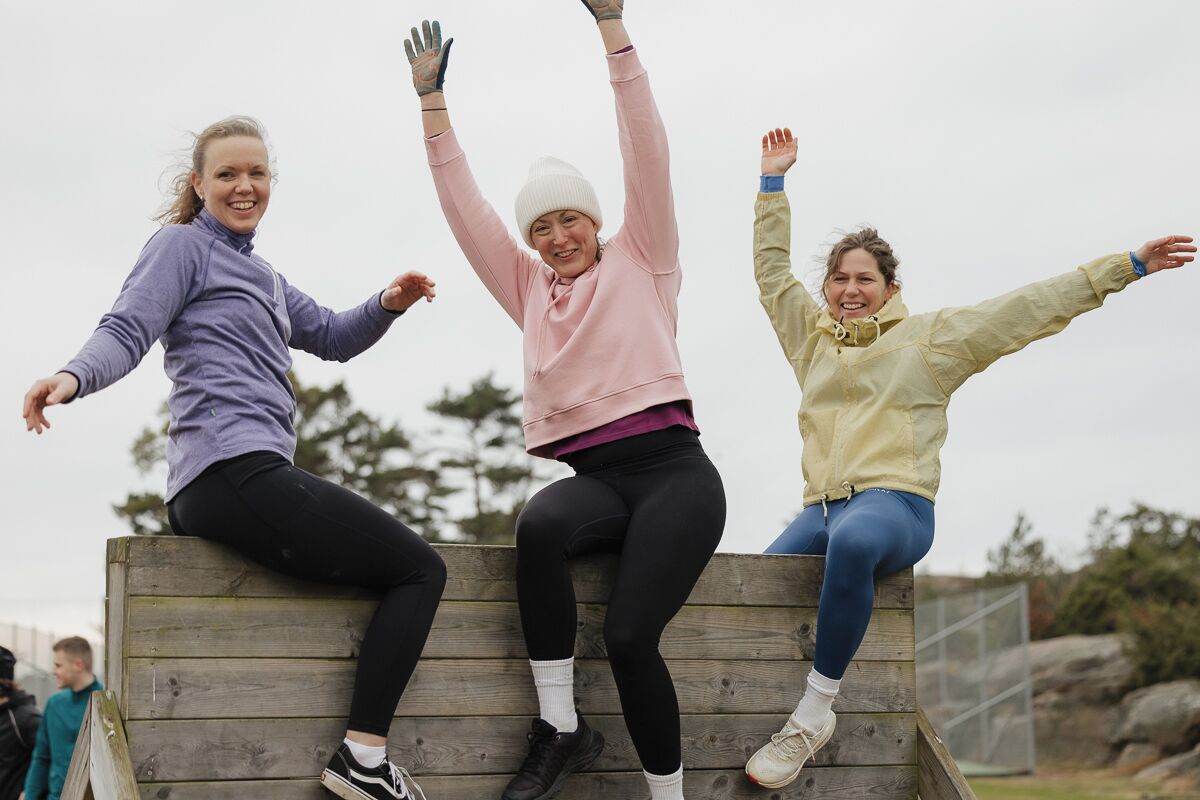 Drie personen zitten op een houten bank buiten.