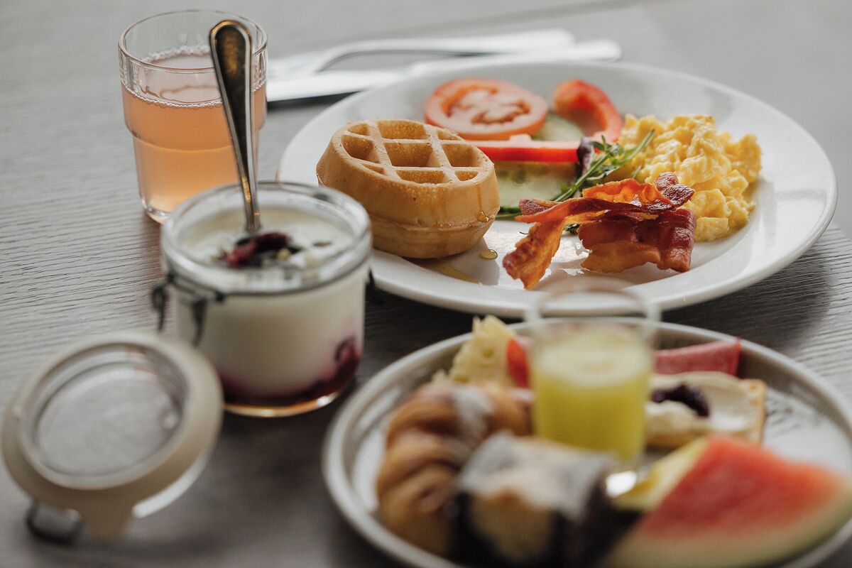 A breakfast plate with waffles, scrambled eggs, bacon, and fruit.