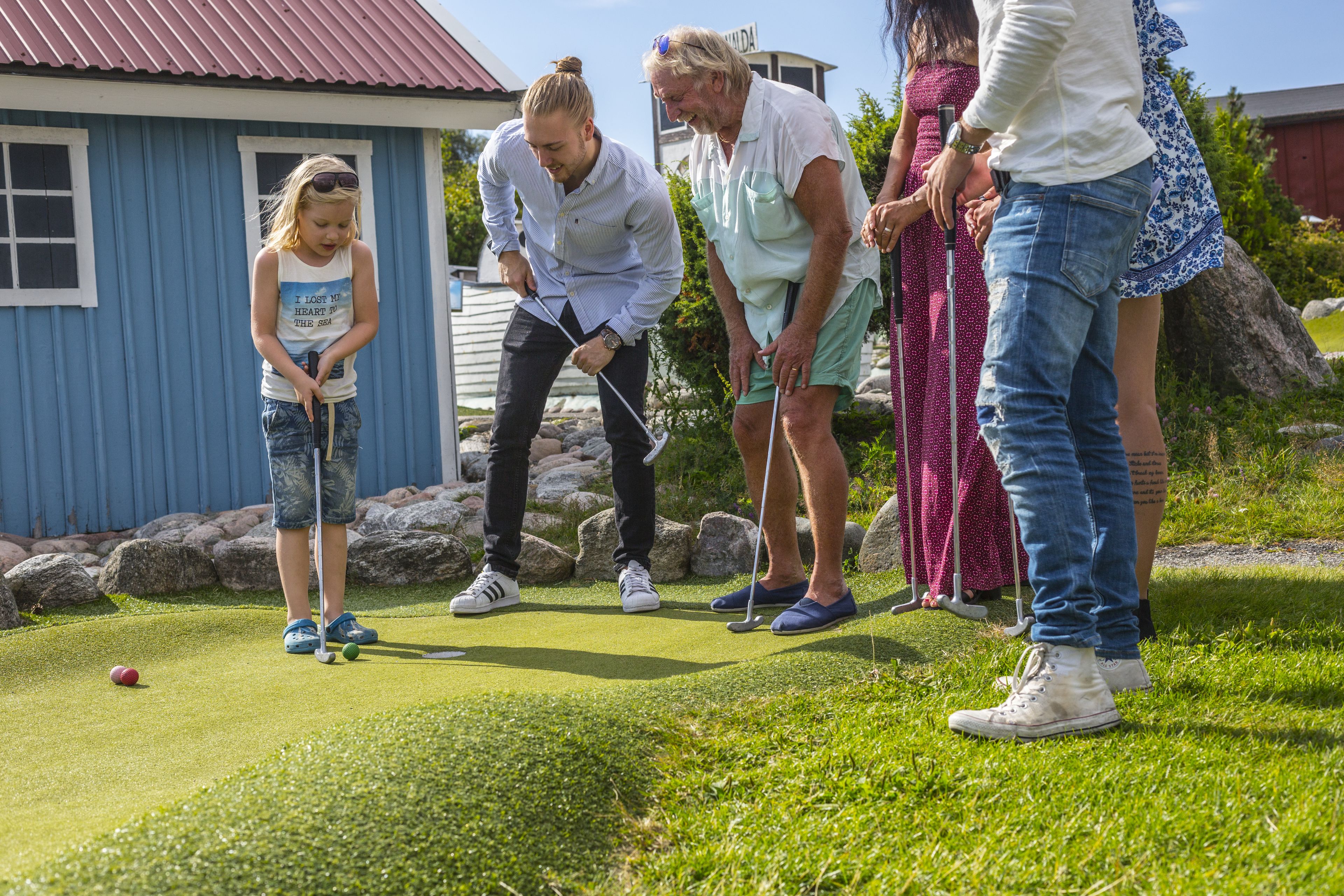 Un grupo de personas jugando golf en un campo verde, con un edificio azul al fondo.