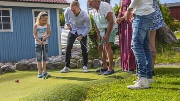 Un grupo de personas jugando golf en un campo verde, con un edificio azul al fondo.