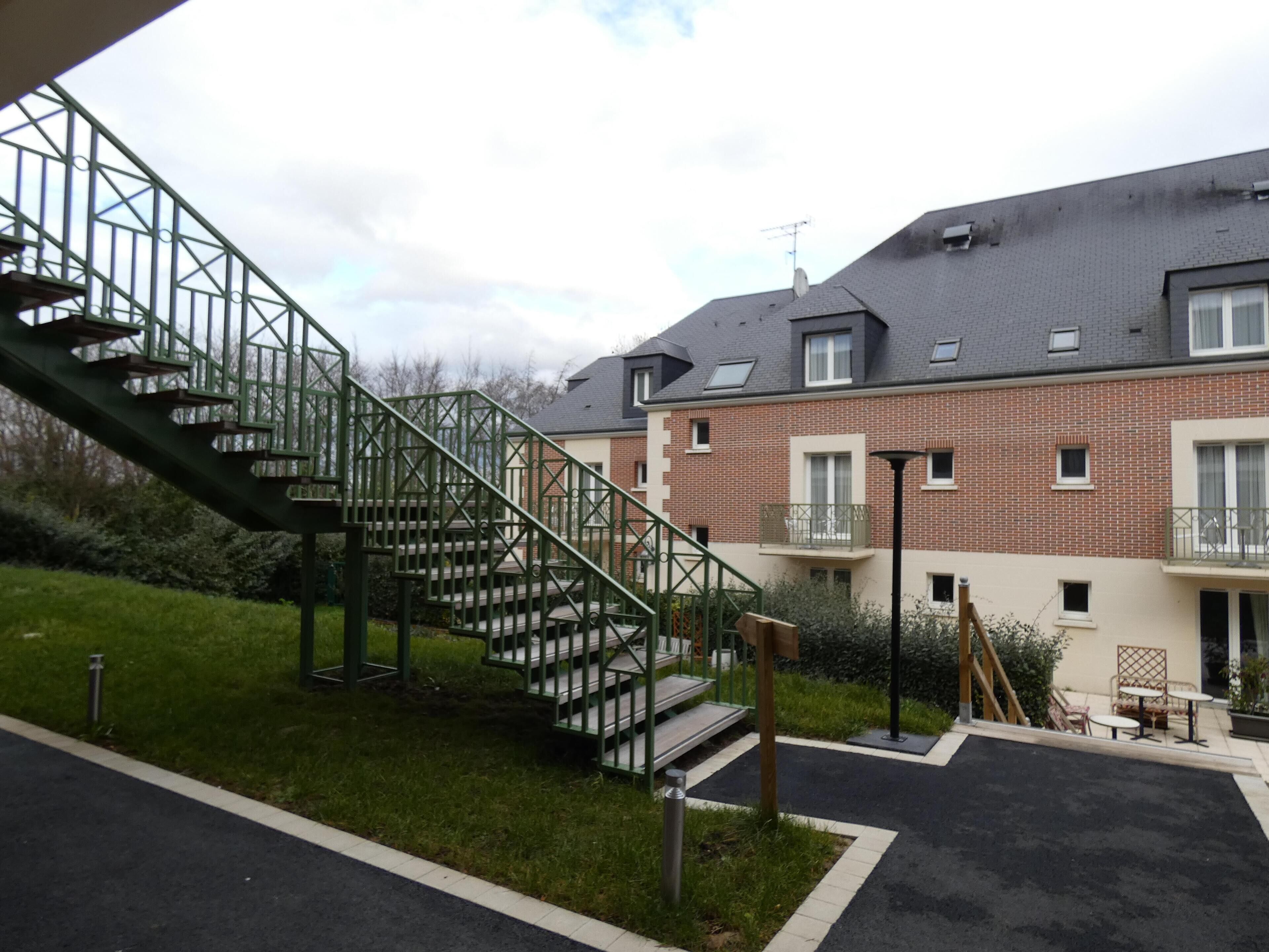 A residential building with a brick facade, multiple windows, and a green staircase leading to a balcony.