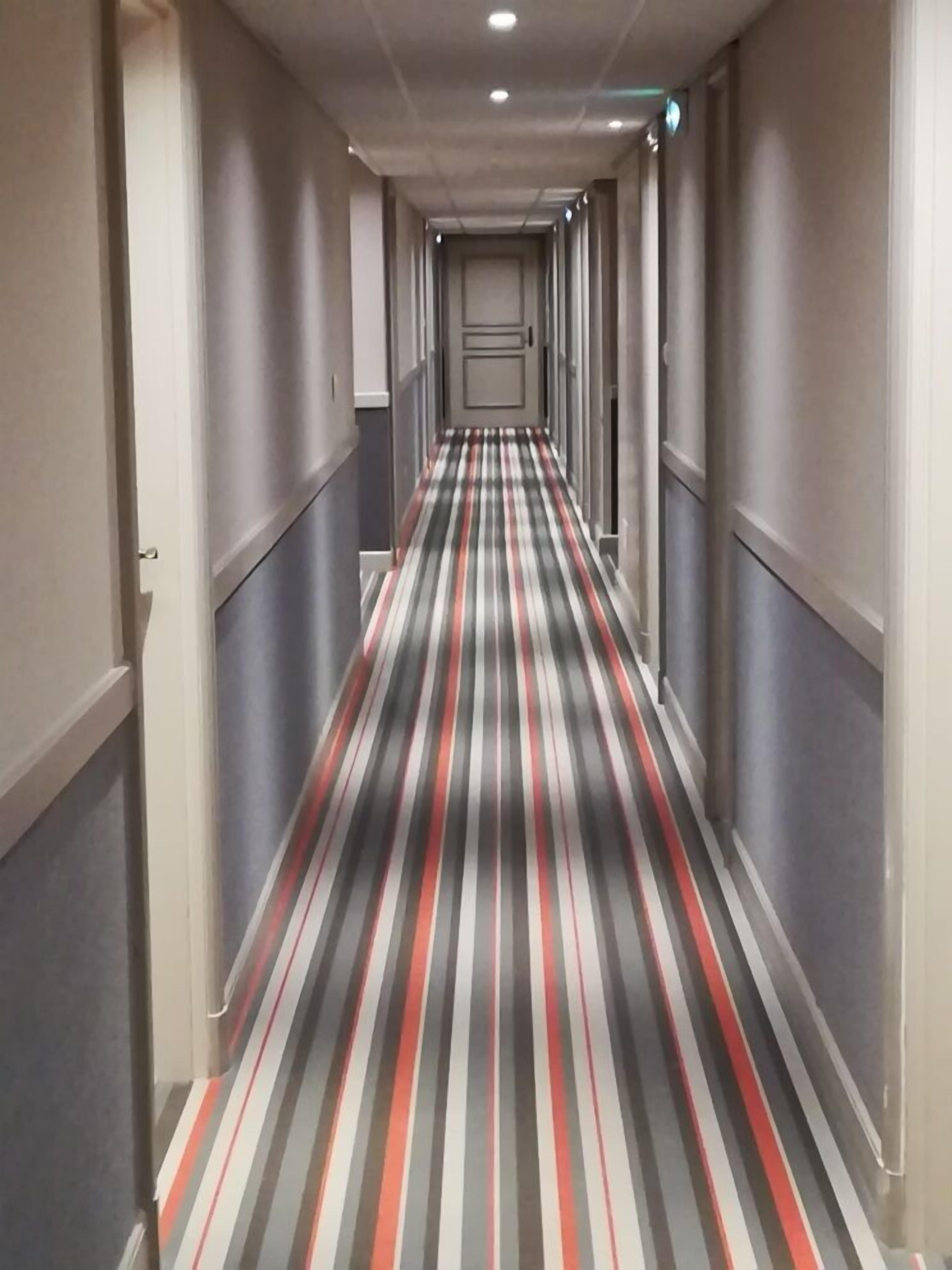 A long, narrow hallway with a striped carpet and a door at the end.