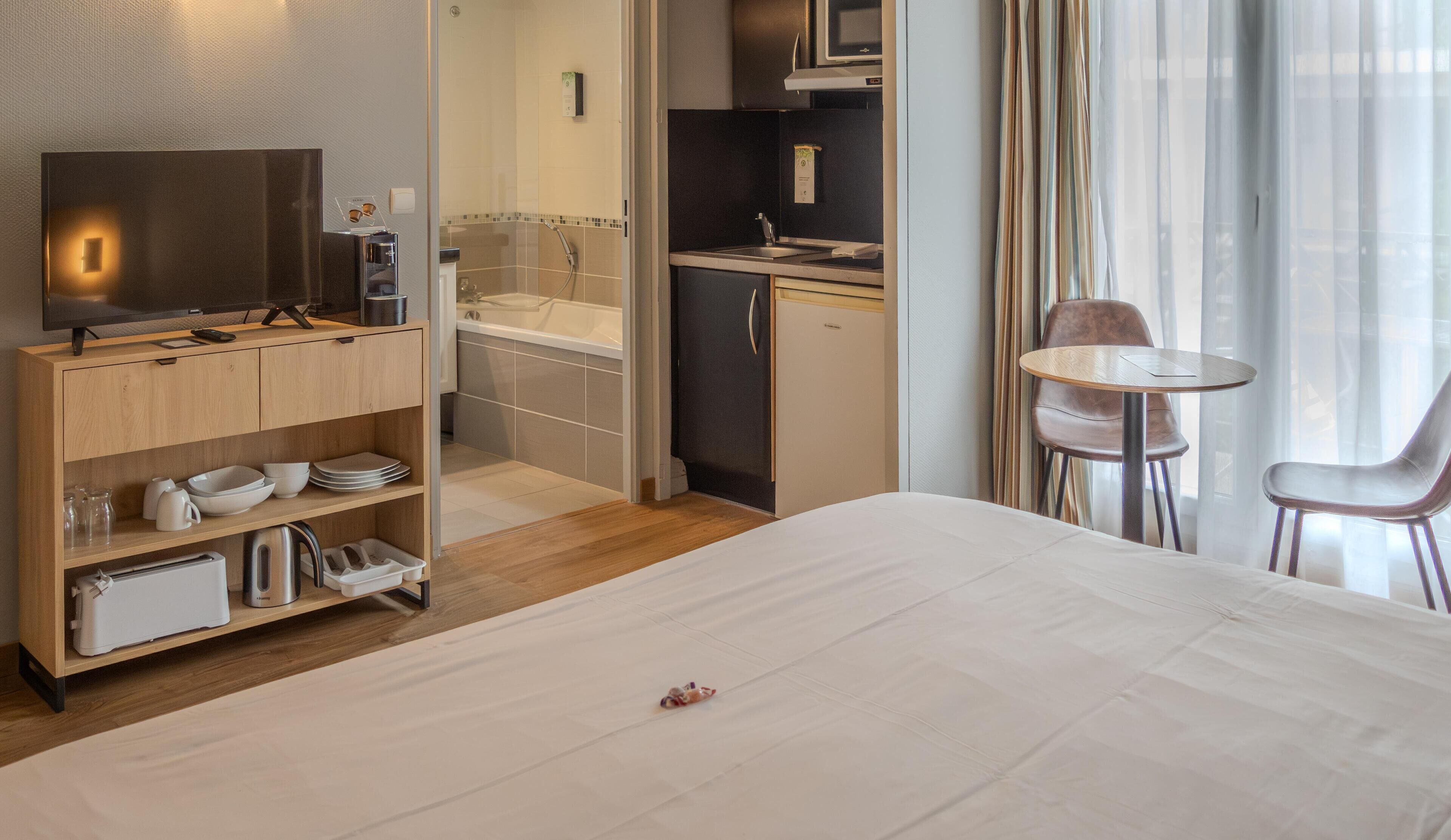 Une chambre d’hôtel comprenant un lit, une télévision, un coin cuisine, une salle de bain et un espace repas avec deux chaises.
