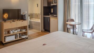 Une chambre d’hôtel comprenant un lit, une télévision, un coin cuisine, une salle de bain et un espace repas avec deux chaises.