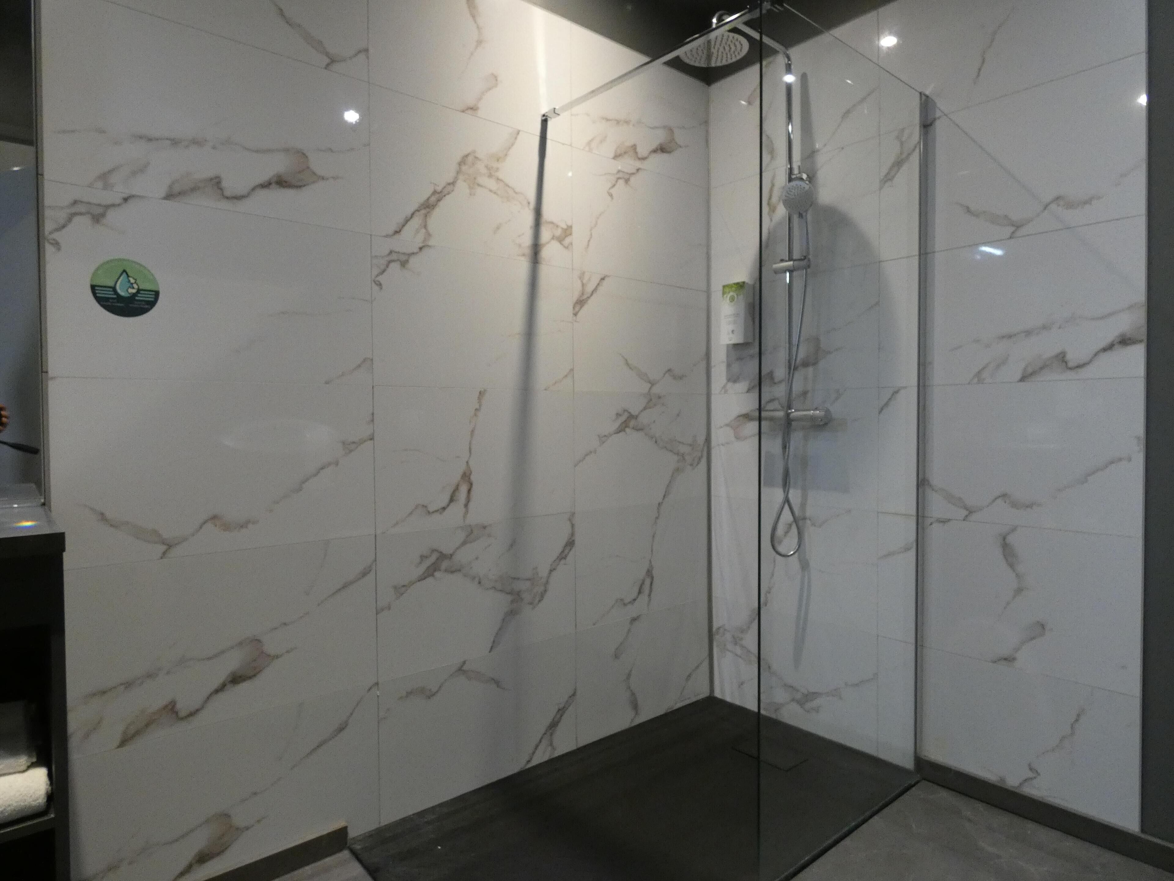 A glass-enclosed shower with a marble wall, a dark floor, and a visible control panel.