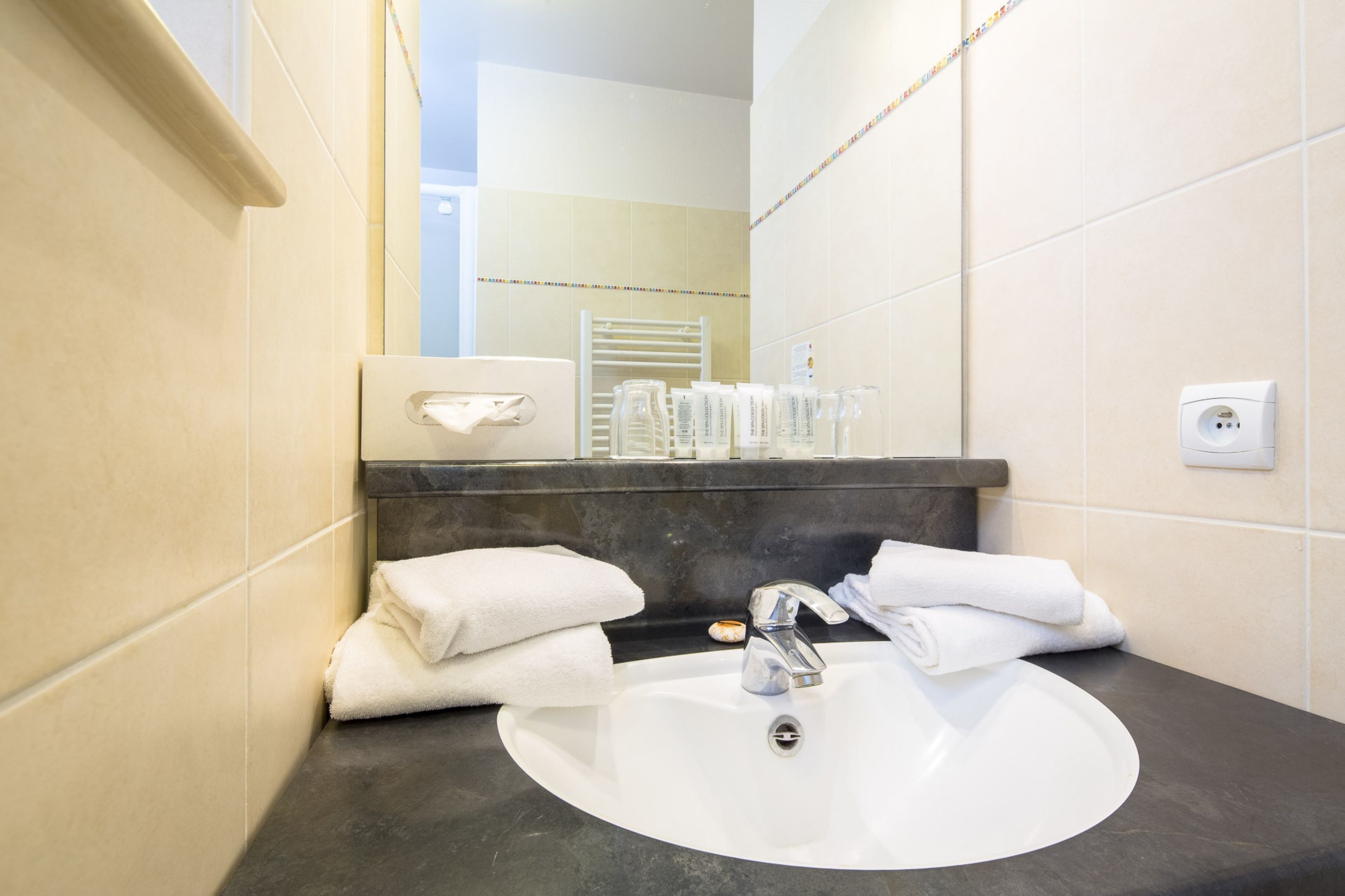 Une salle de bain avec un lavabo blanc, un plan de toilette foncé et un porte-serviettes.