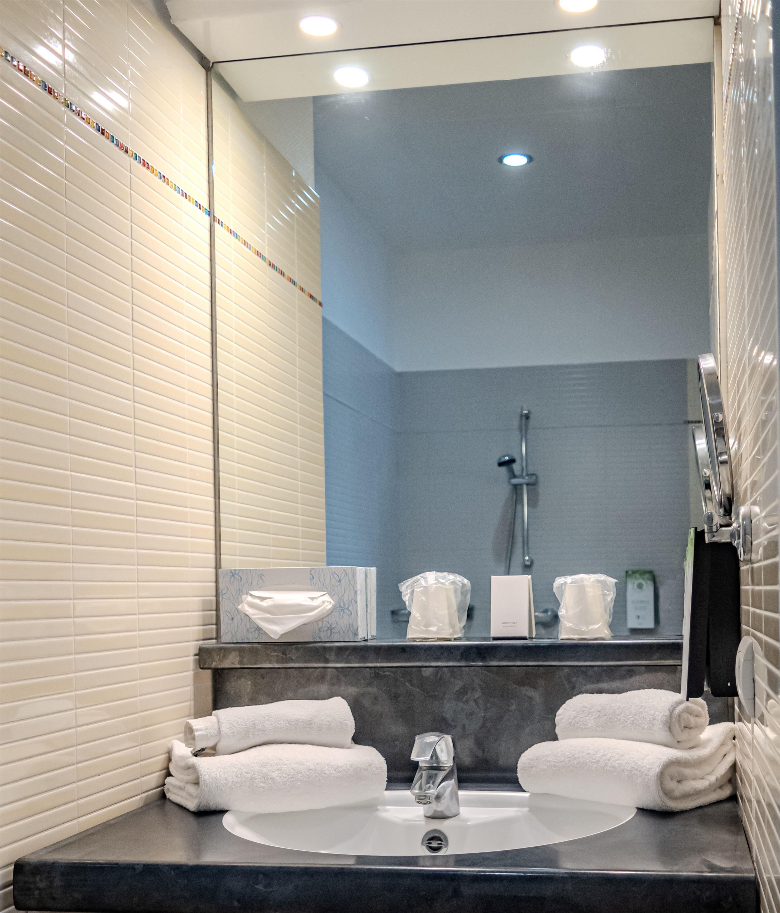 A modern bathroom with a large mirror, a sink with two towels, and a shower area.