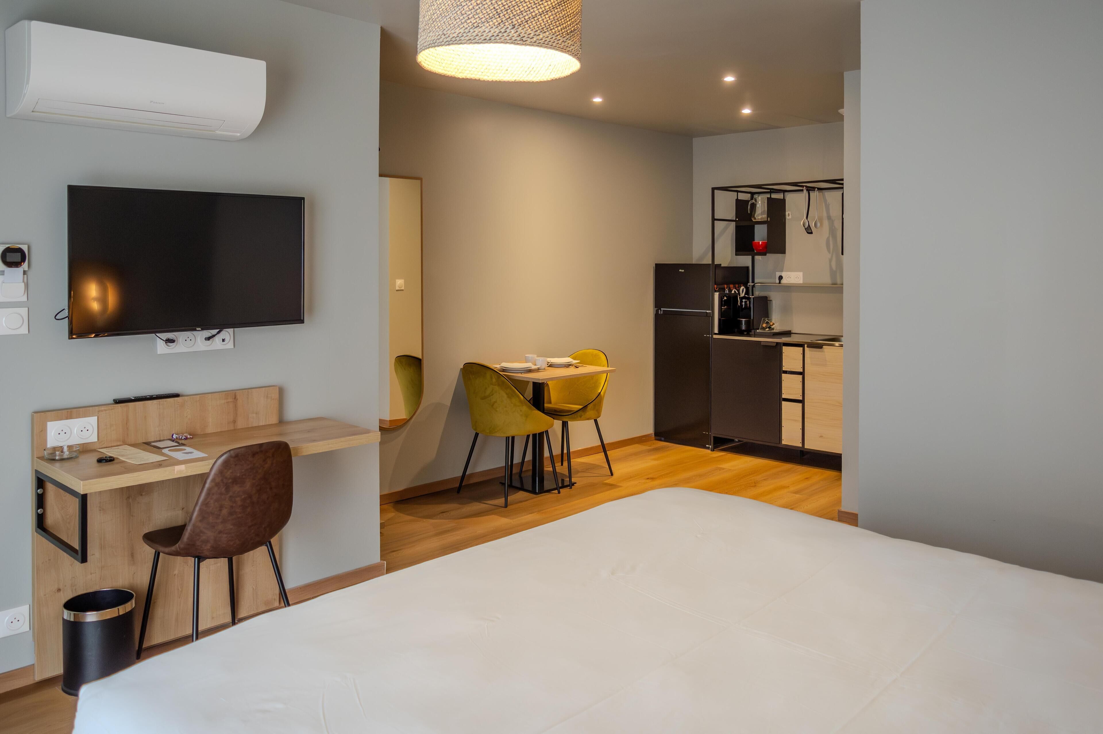 Una habitación de hotel moderna con una cama, un escritorio con silla, televisor y kitchenette.