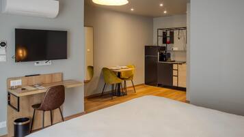 A modern hotel room with a bed, a desk with a chair, a television, and a kitchenette.