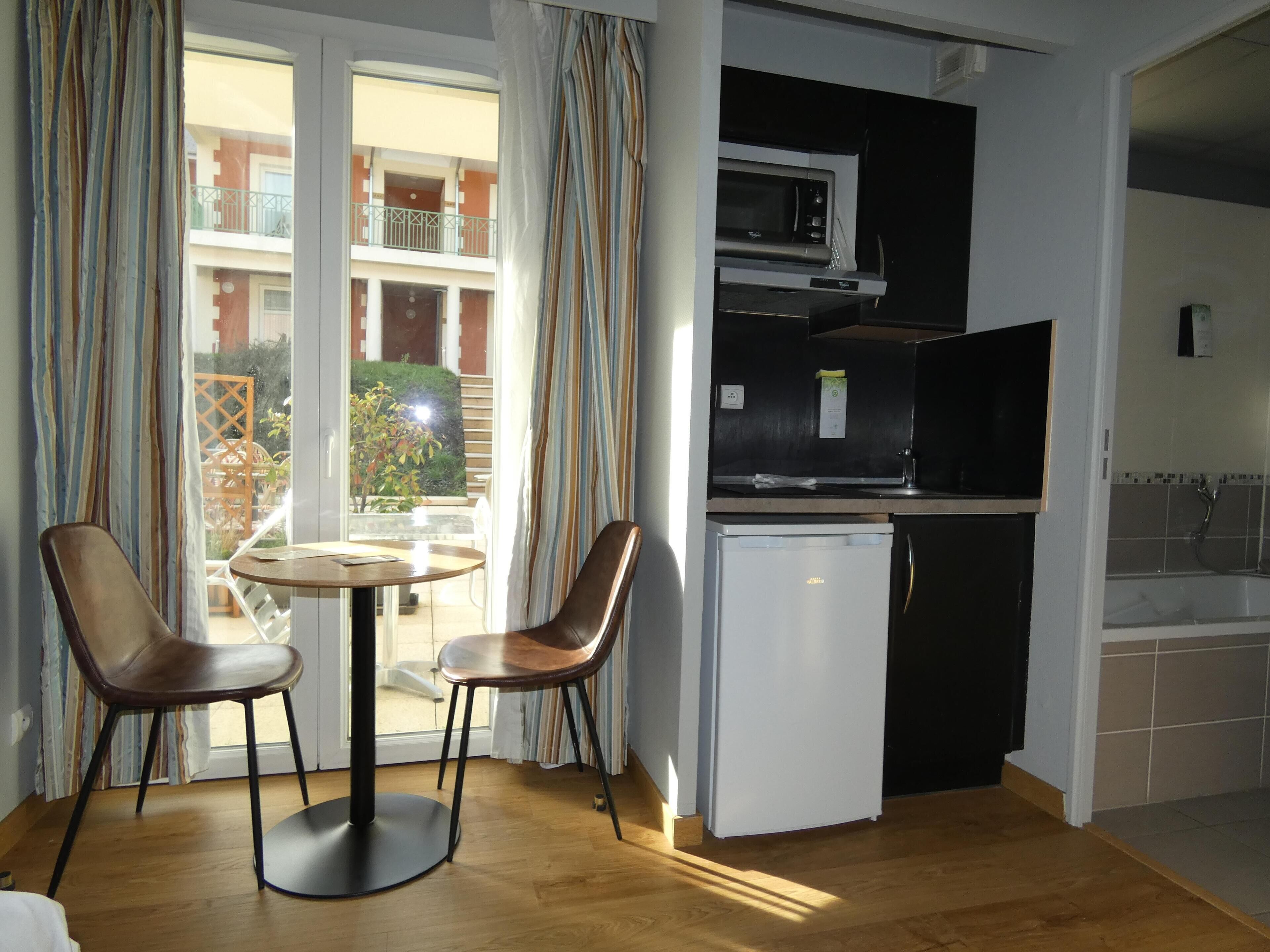 Een compacte keuken met een magnetron, koelkast, en een eethoekje met twee stoelen en een tafel.