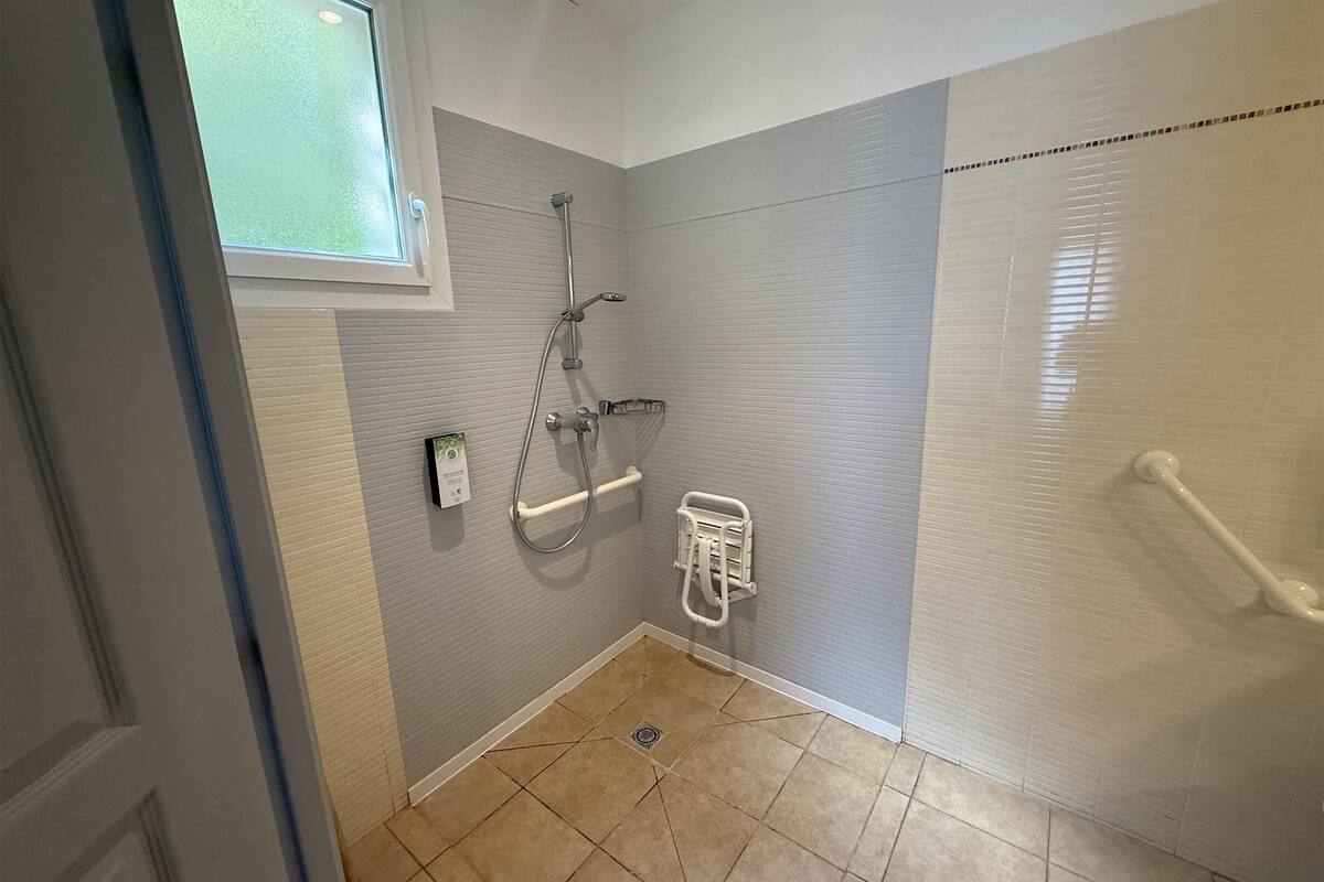 Uma casa de banho pequena e moderna com chuveiro, apoio de segurança e janela.