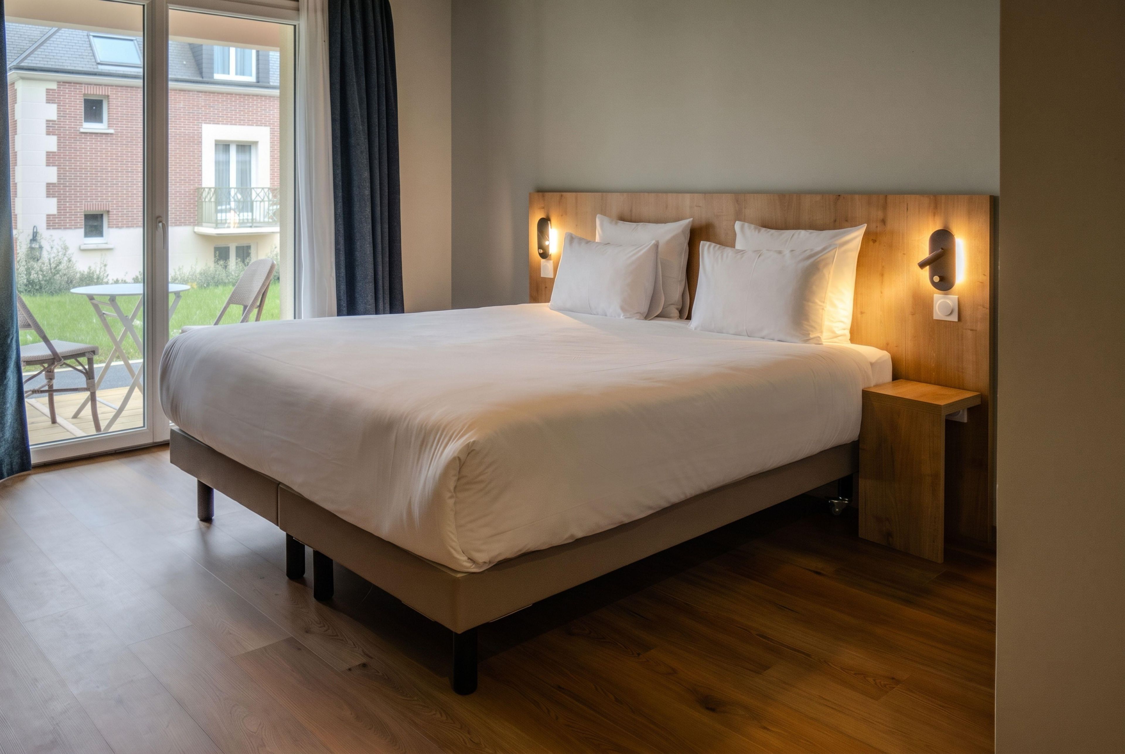 A hotel room with a large bed, wooden headboard, bedside tables, and a view of a balcony.