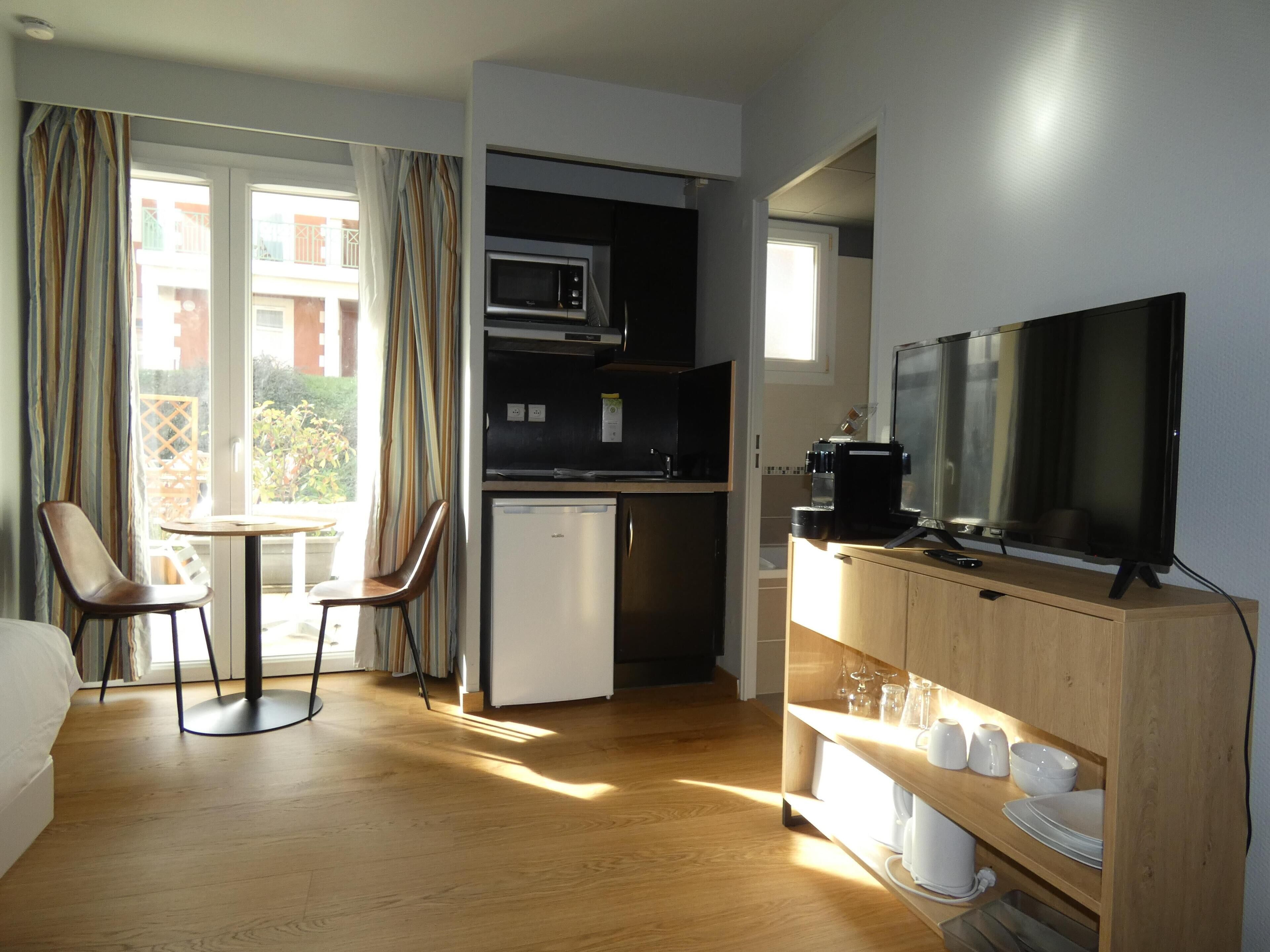 Ein kompaktes Hotelzimmer mit Küchenzeile, einem Essbereich mit Tisch und Stühlen, einem Fernseher und einem kleinen Kühlschrank.