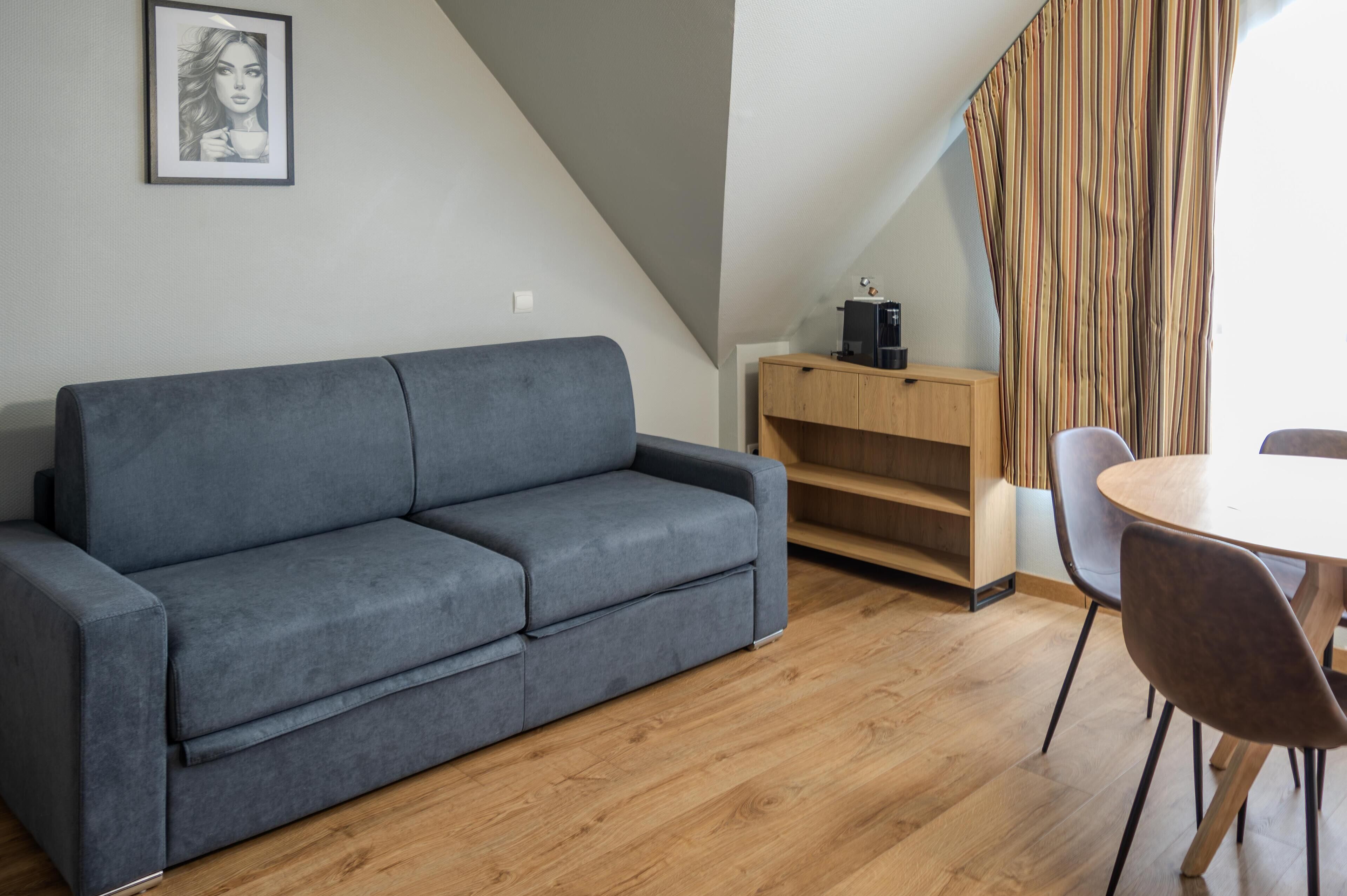 Una sala de estar moderna con un sofá gris, suelo de madera, una mesa de comedor con sillas, una cafetera y una cortina a rayas.