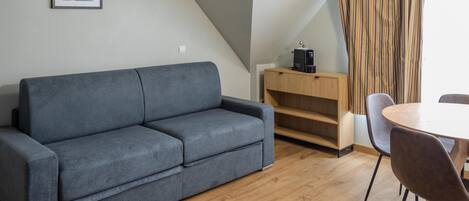 Una sala de estar moderna con un sofá gris, suelo de madera, una mesa de comedor con sillas, una cafetera y una cortina a rayas.