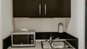 Une cuisine de taille réduite, équipée d’un four à micro-ondes, d’un évier et de meubles de rangement de couleur sombre.