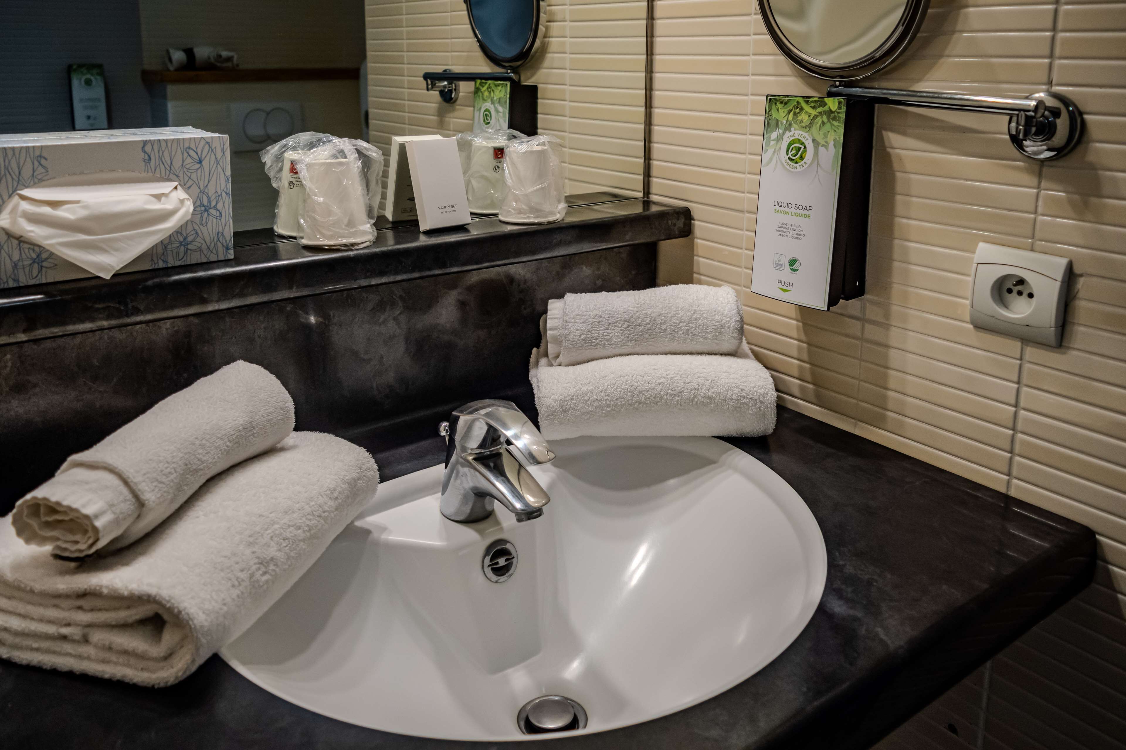 A bathroom with a white sink, two towels, a mirror, and toiletries on the counter.