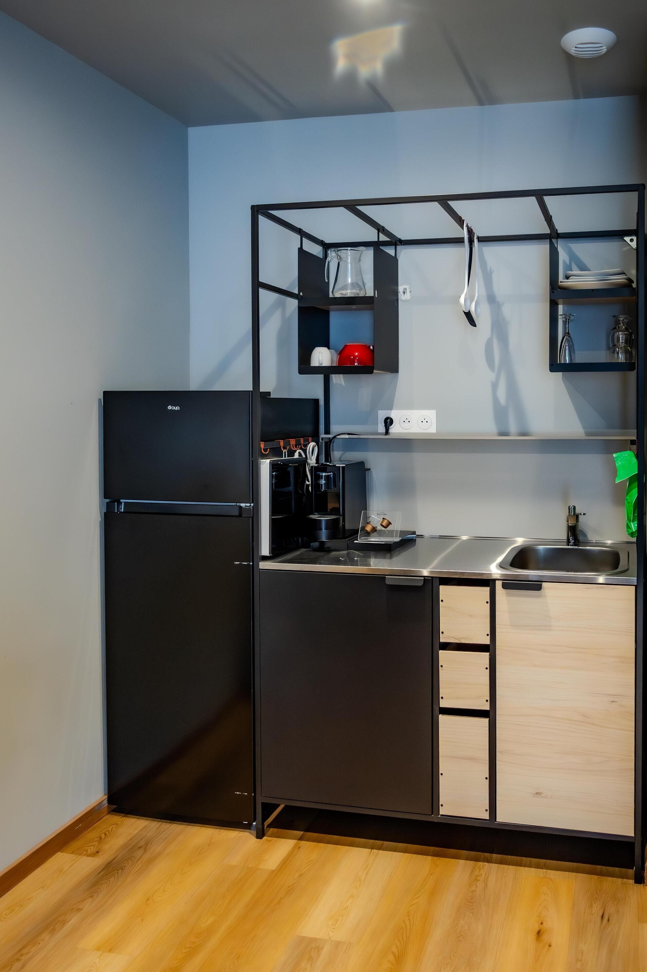 A compact kitchen with a black refrigerator, a coffee machine, and a sink.