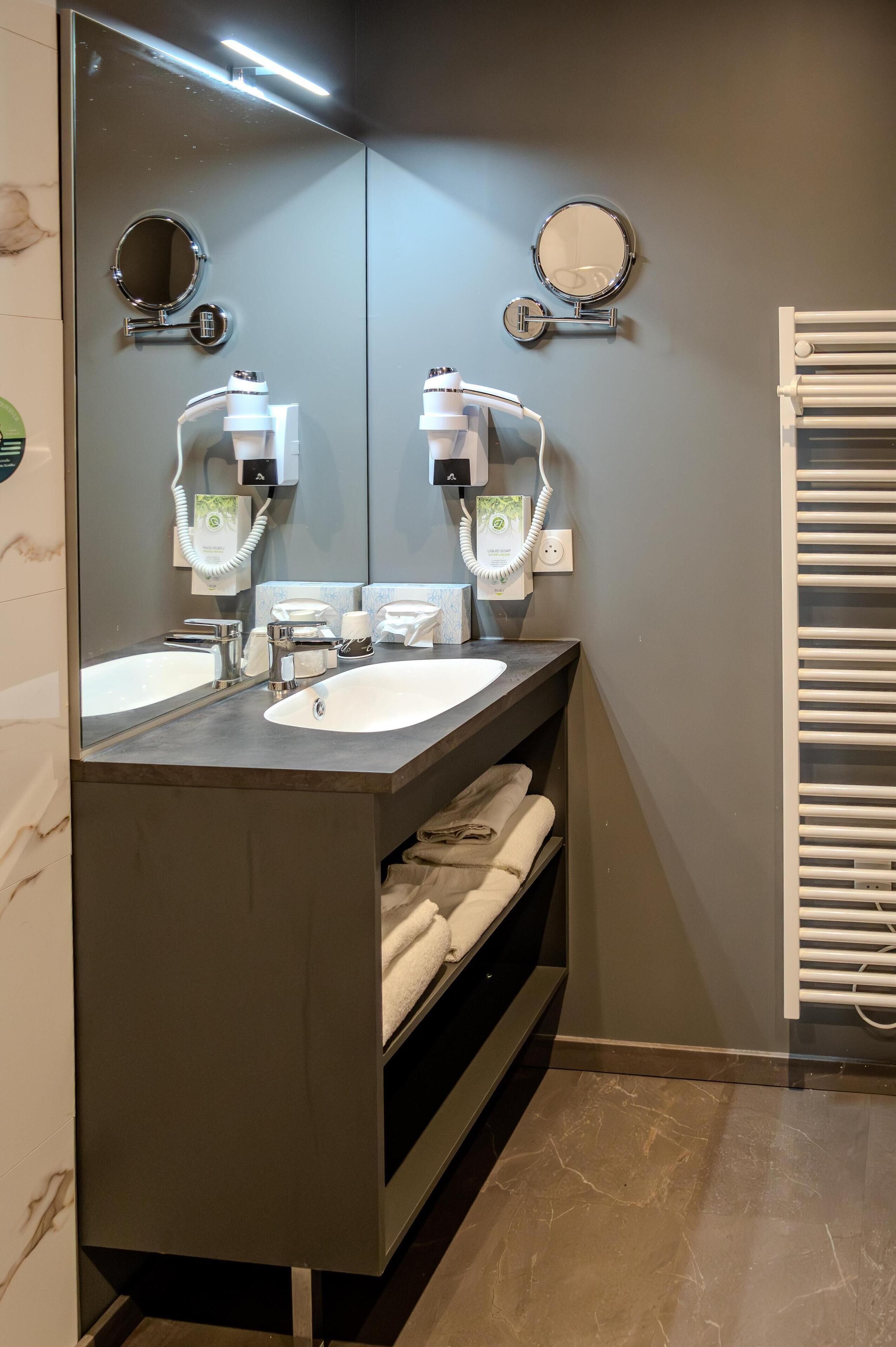 A modern bathroom with two sinks, a large mirror, and a towel rack.