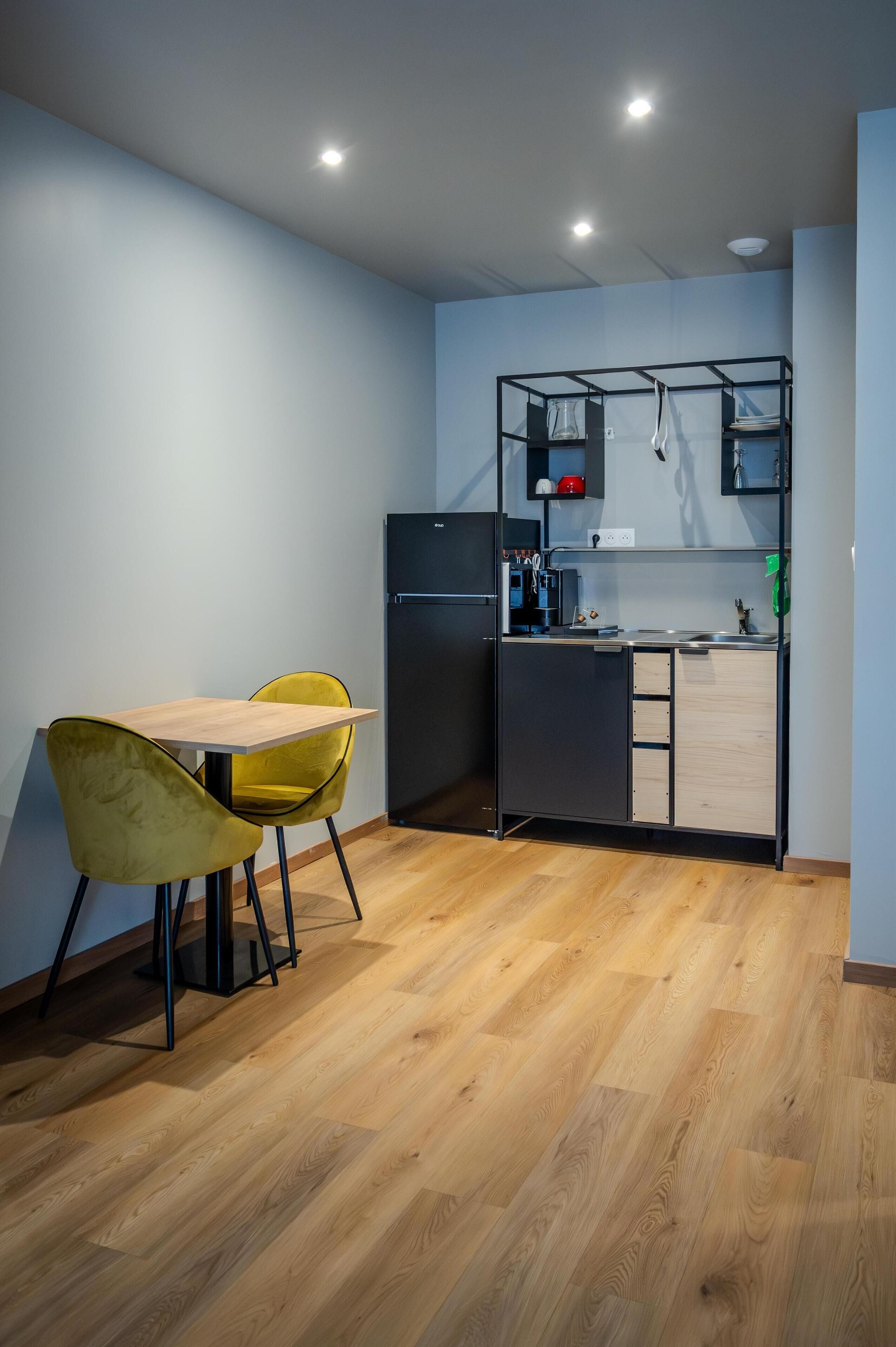 Una cucina compatta con tavolo e sedie, un frigorifero integrato e un piccolo piano di lavoro con lavello.