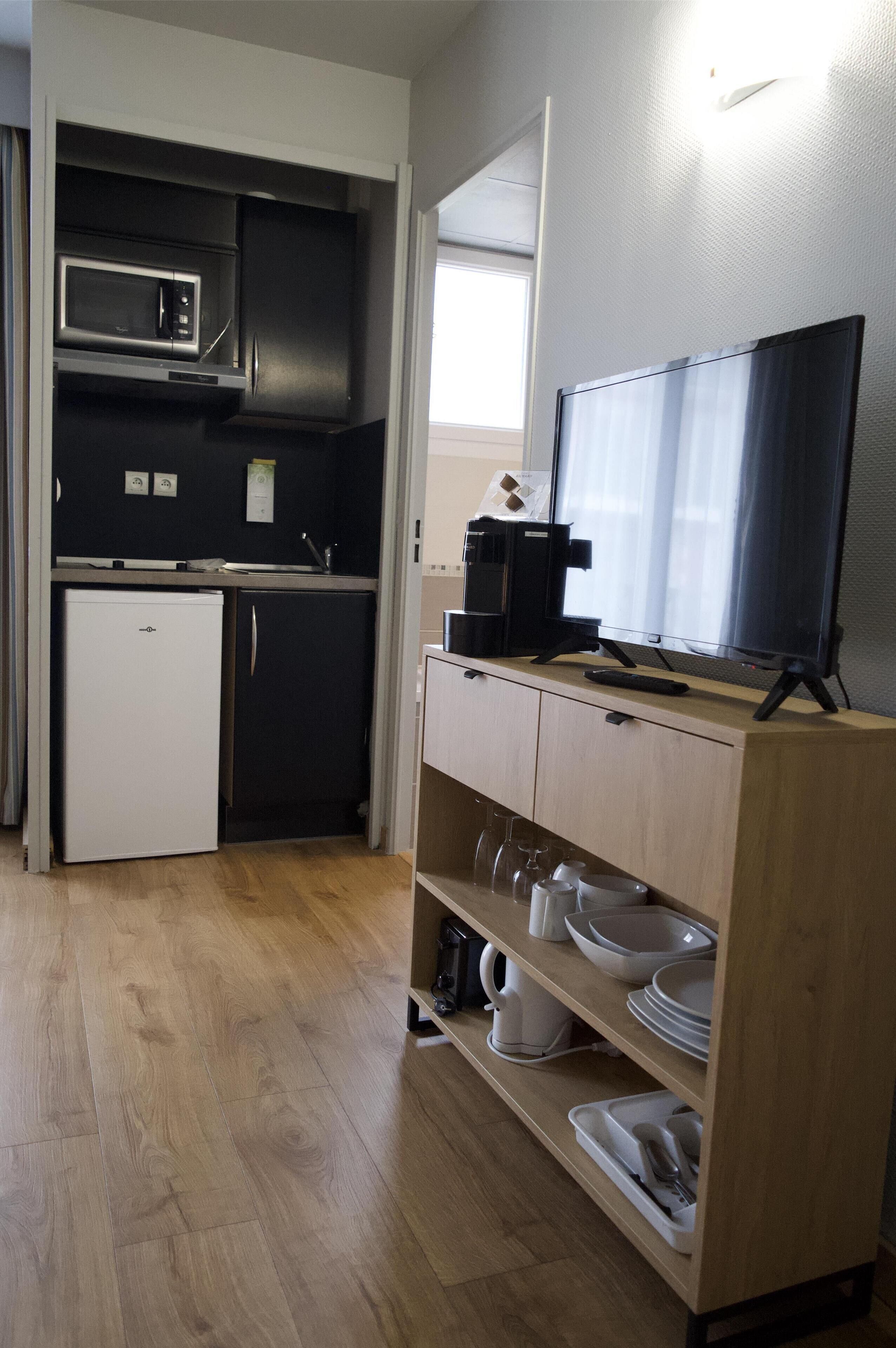 Een kleine keuken met een magnetron, koffiezetapparaat en een televisie op een houten kast.