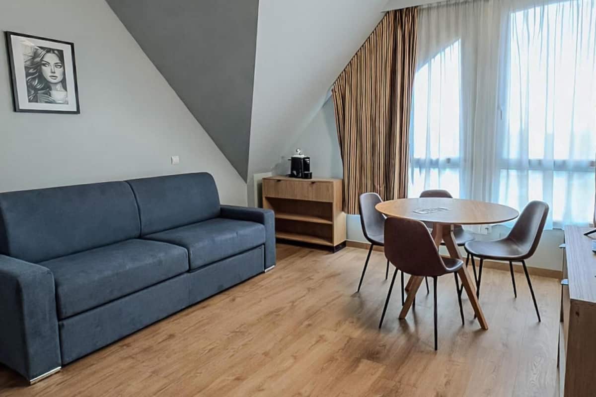 Uma sala de estar moderna com um sofá, uma mesa de jantar com cadeiras, uma cafeteira e uma estante de livros.