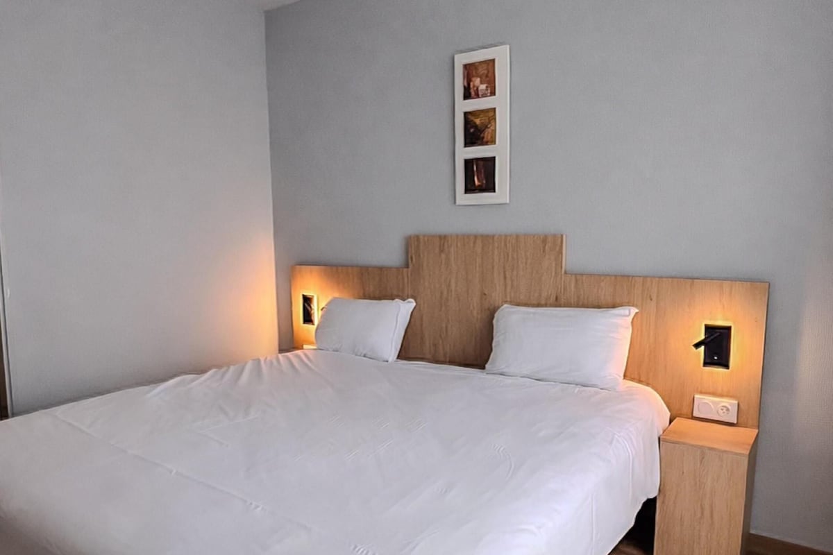 Una cama grande con sábanas blancas, cabecera de madera y lámparas de noche.