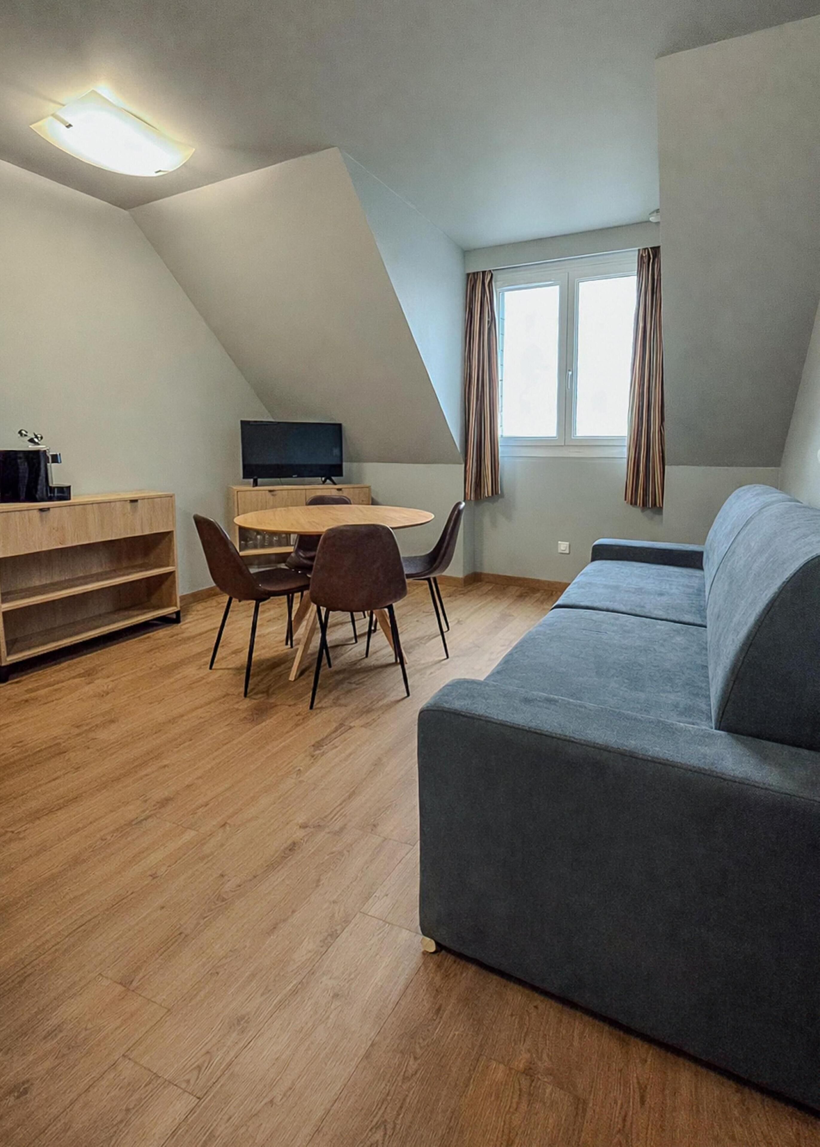 Een moderne loftkamer met een eethoek, een bank, een televisie en een raam met gordijnen.
