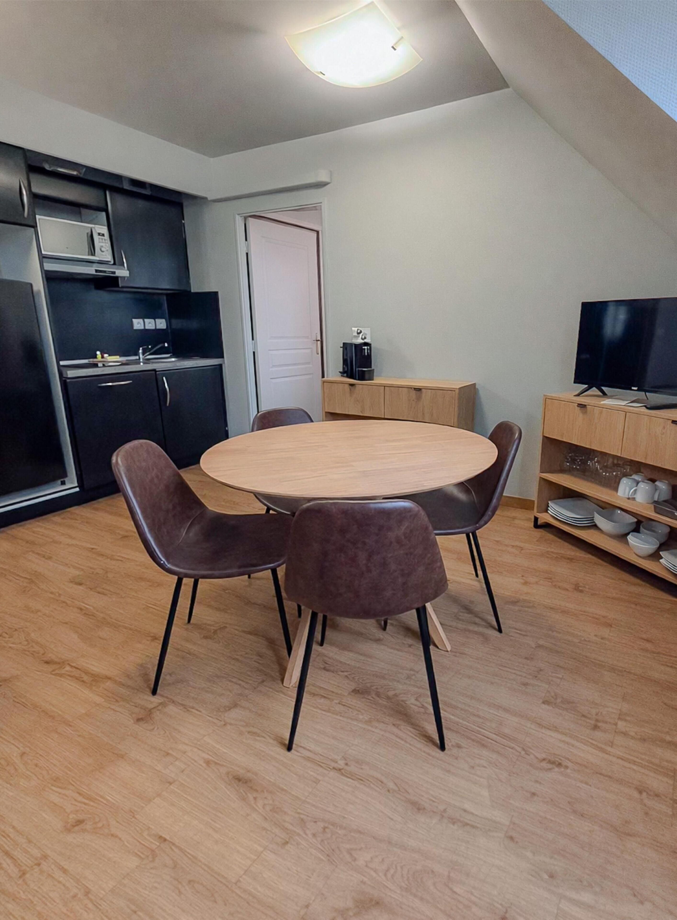 A compact kitchen with a dining area, a flat-screen TV, and a coffee machine.