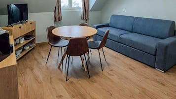 A modern living room with a round wooden table, four chairs, a blue sofa, and a television on a wooden stand.
