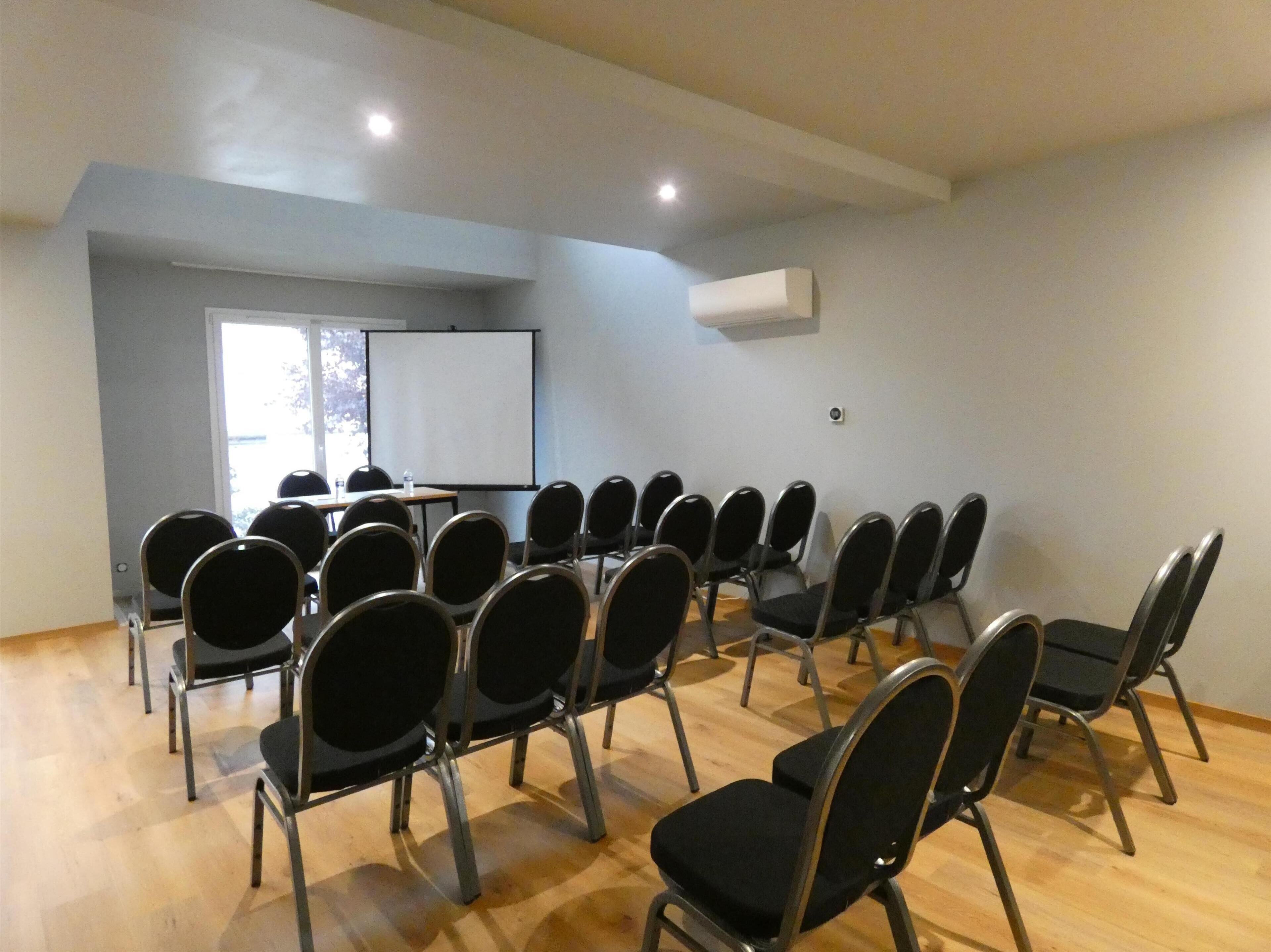 Ein Konferenzraum mit Stuhlreihen, einer Whiteboard-Tafel und einer Projektionsleinwand.