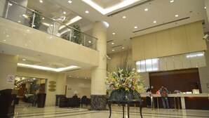Um hall amplo com balcão de recepção, área de estar e um arranjo floral decorativo.