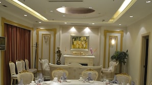 Uma mesa de jantar redonda posta para uma refeição, com cadeiras ao redor, um candelabro acima e um quadro na parede.