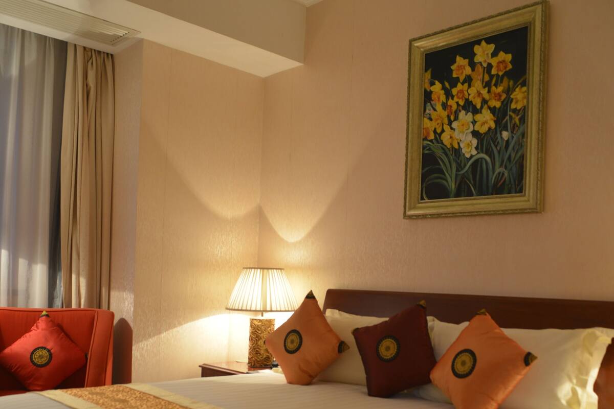 A hotel room with a large bed, a nightstand, a lamp, and a painting on the wall.