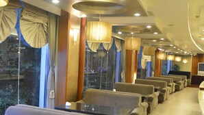 Um saguão de hotel com fileiras de assentos, janelas amplas e luminárias modernas.