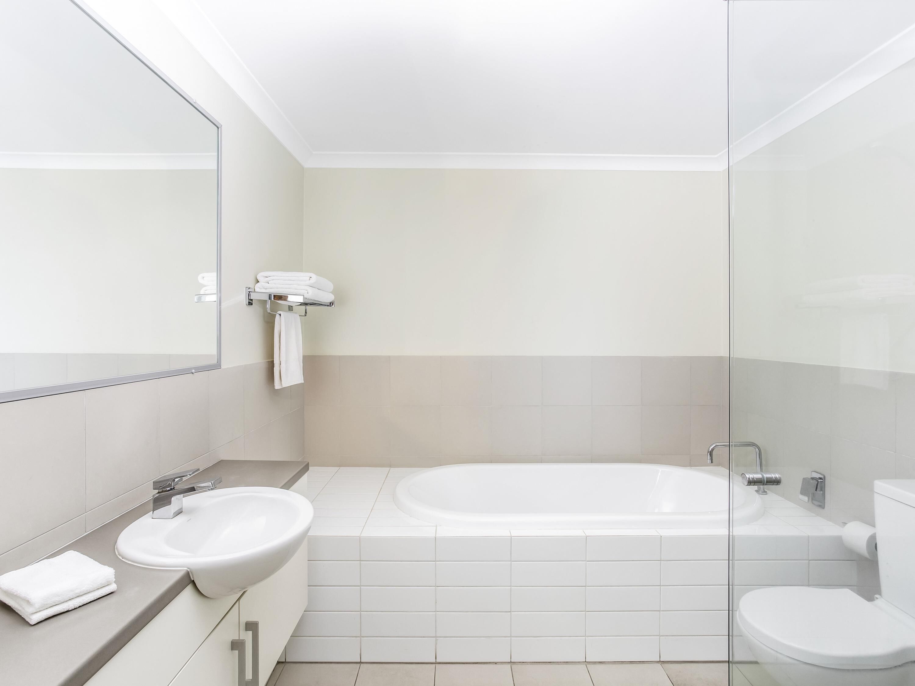 A modern bathroom with a bathtub, two sinks, a toilet, and a glass shower enclosure.