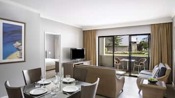 A hotel room with a dining area, a television, a balcony with a view of the outside, and a bed.