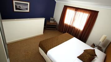 Une chambre d’hôtel avec un lit, un téléviseur posé sur un meuble, une fenêtre avec des rideaux et un tableau encadré au mur.