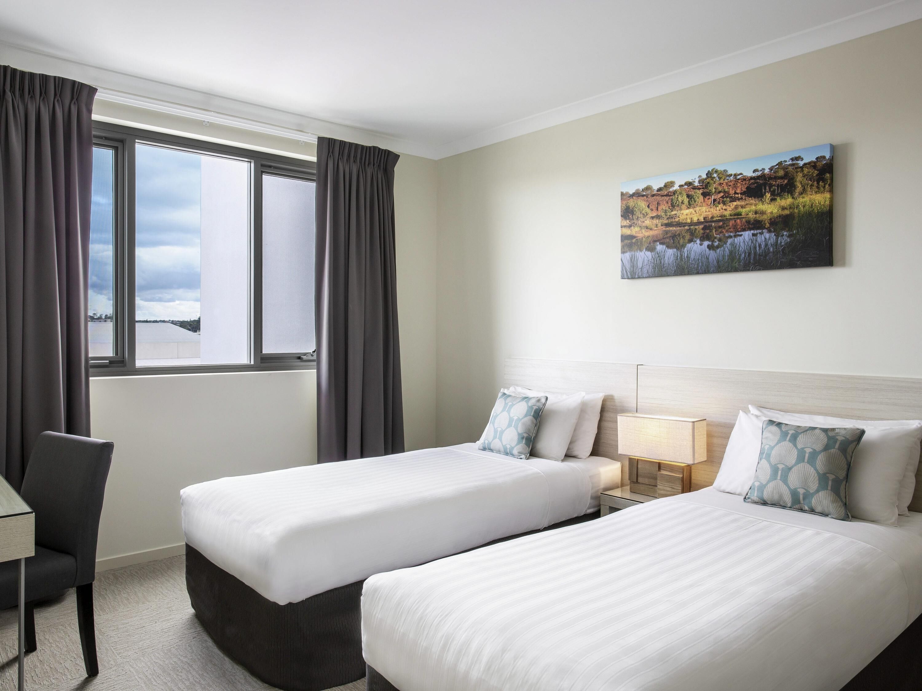 Ein Hotelzimmer mit zwei Betten, einem Schreibtisch und einem Fenster mit Vorhängen.