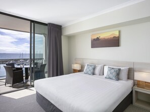Habitación de hotel con una cama grande, dos mesitas de noche, vista al puerto deportivo y un cuadro en la pared.