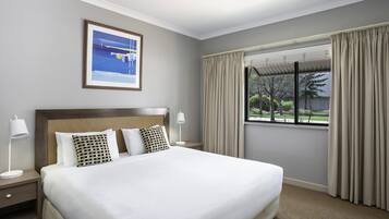 A hotel room with a large bed, a nightstand, a lamp, a framed picture on the wall, and a window with curtains.