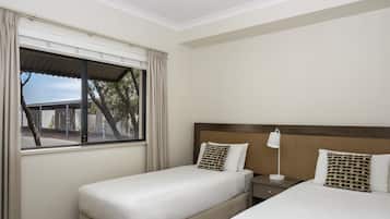 Habitación de hotel con dos camas, una mesita de noche, una lámpara y una ventana con cortinas.
