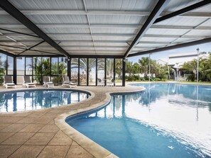 Piscina con sillas de descanso y una zona cubierta con ventanales amplios.