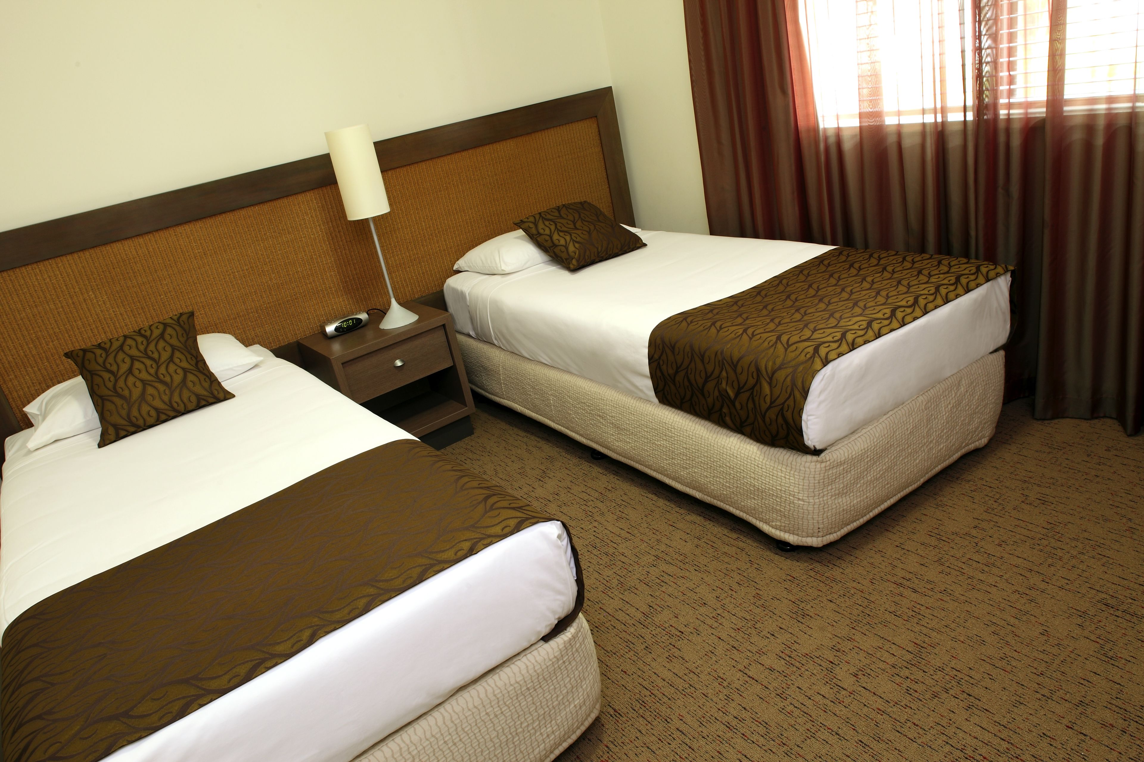 Two twin beds with brown and white bedding, a bedside table with a lamp, and a window with curtains.