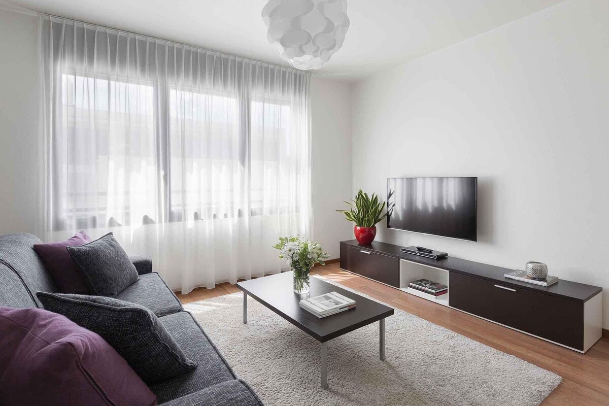Una sala de estar moderna con sofá, mesa de centro, televisor y una planta.